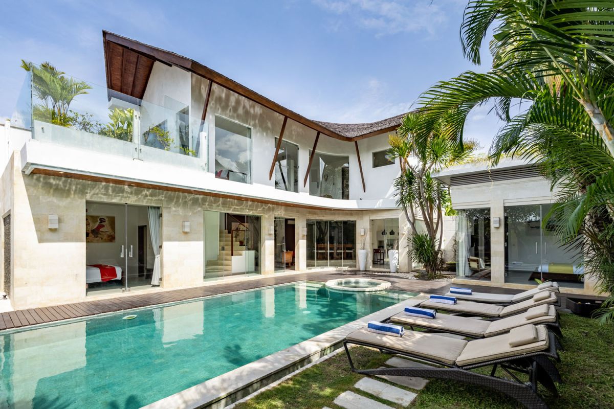 Modern white Bali villa with infinity pool, lounge chairs, and lush tropical garden. - Bali Villas