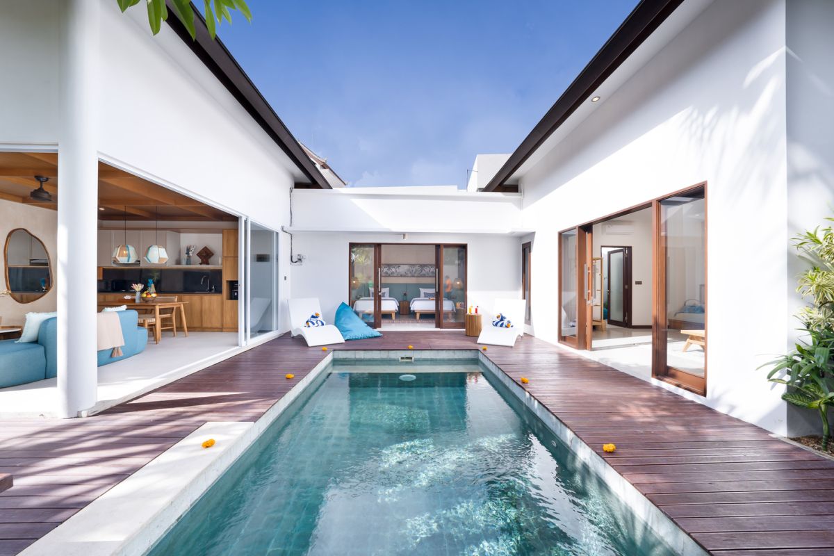 Modern Balinese villa with turquoise infinity pool, wooden deck, white walls, and open indoor-outdoor living space. - Bali Villas