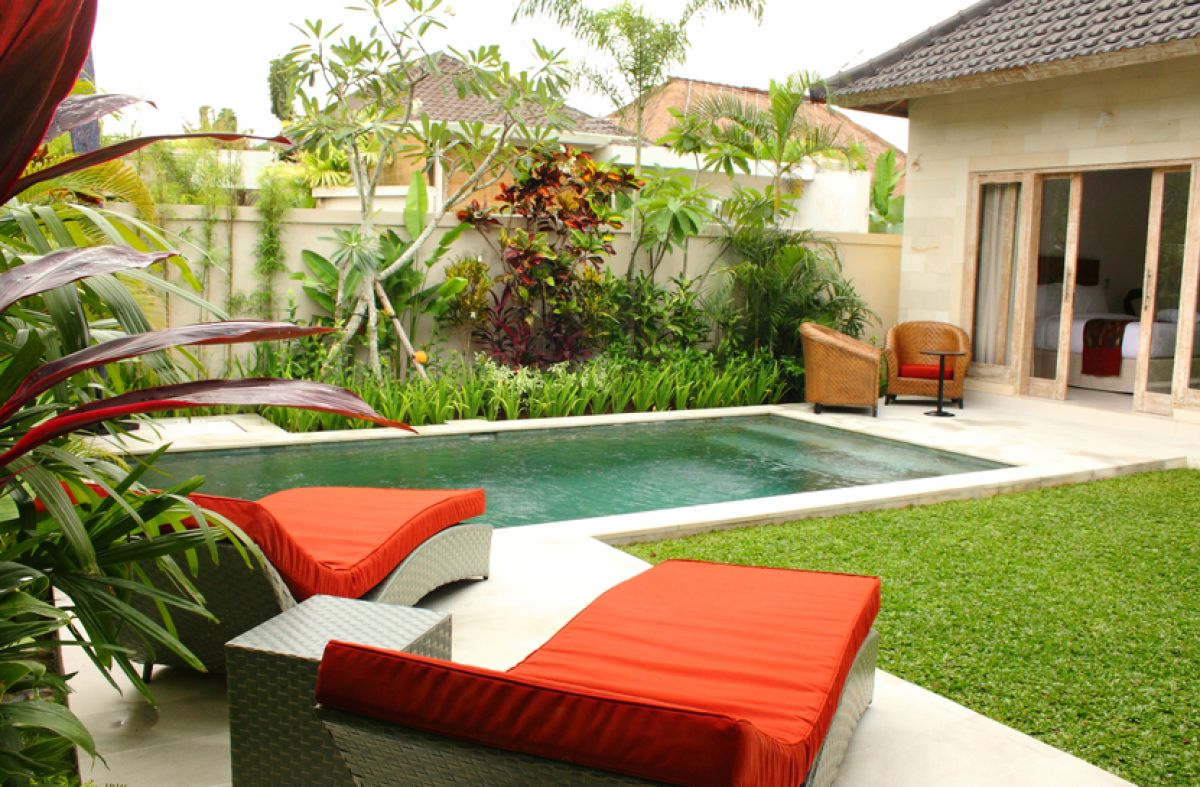 Serene private infinity pool in a lush tropical Balinese villa garden, with red lounge chairs on a stone patio. - Bali Villas