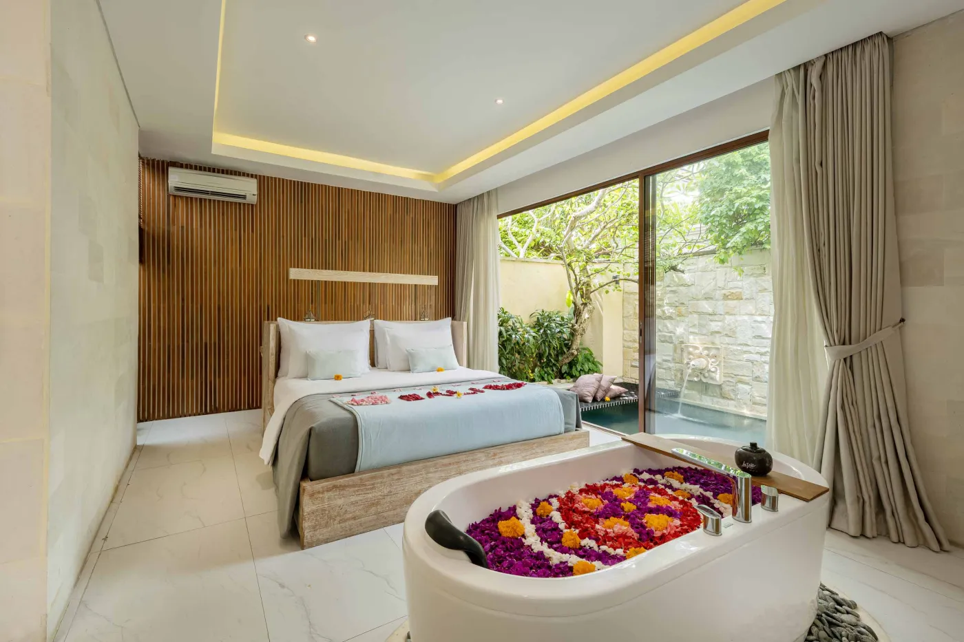 Cozy Balinese villa lounge with wooden paneled walls, gray sofa and chairs around a marble table, abstract wall art, and lush garden window view. - Bali Villas
