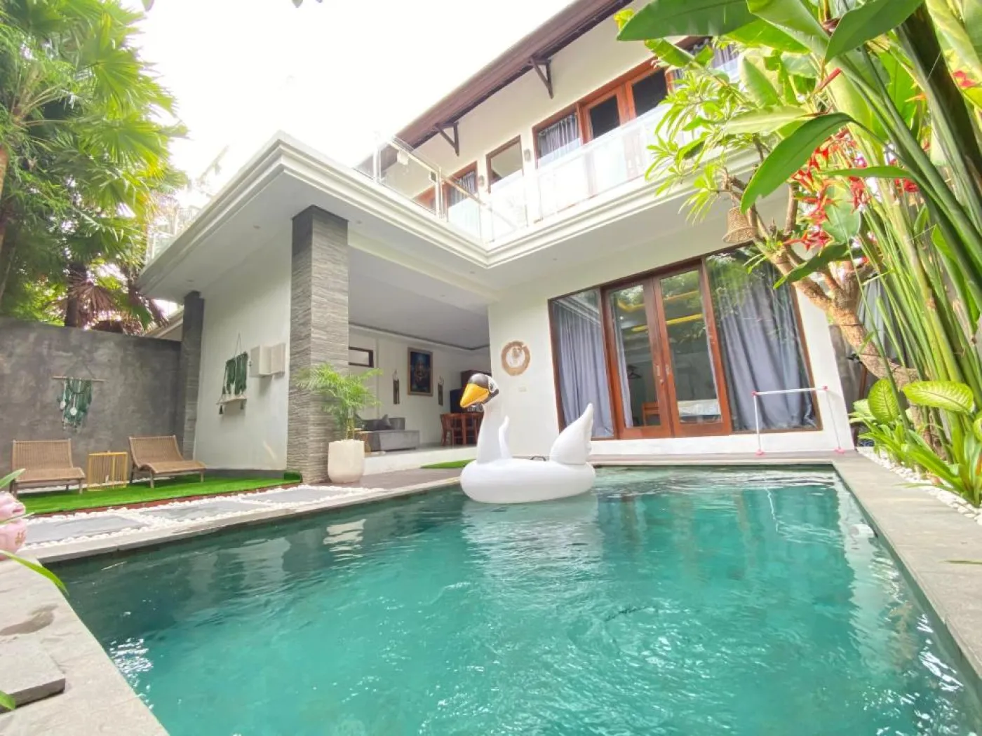 Serene tropical villa pool with white swan float in turquoise water, surrounded by lush greenery and modern Balinese architecture. - Bali Villas