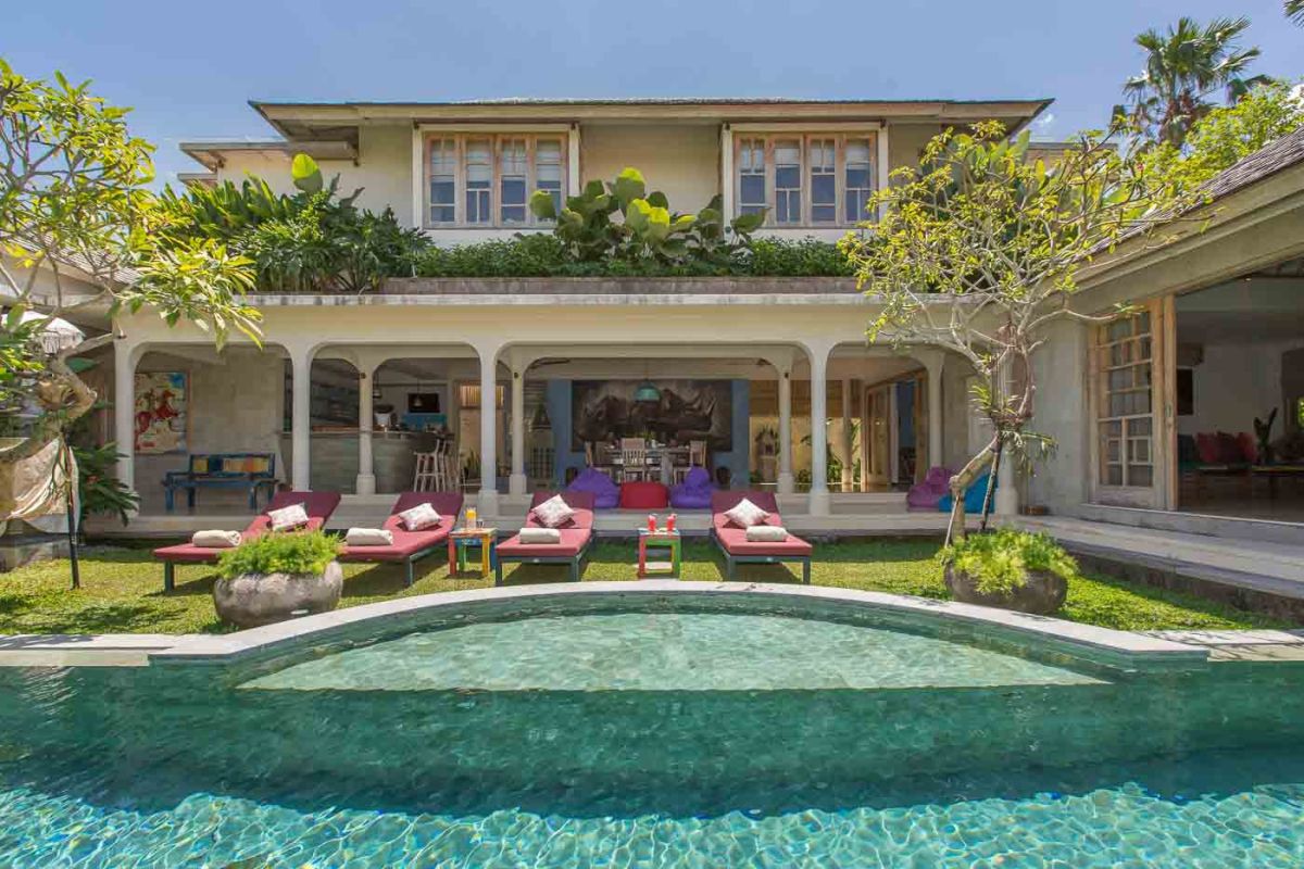 Luxurious Bali villa with curved infinity pool, red lounge chairs, and lush tropical gardens. - Bali Villas