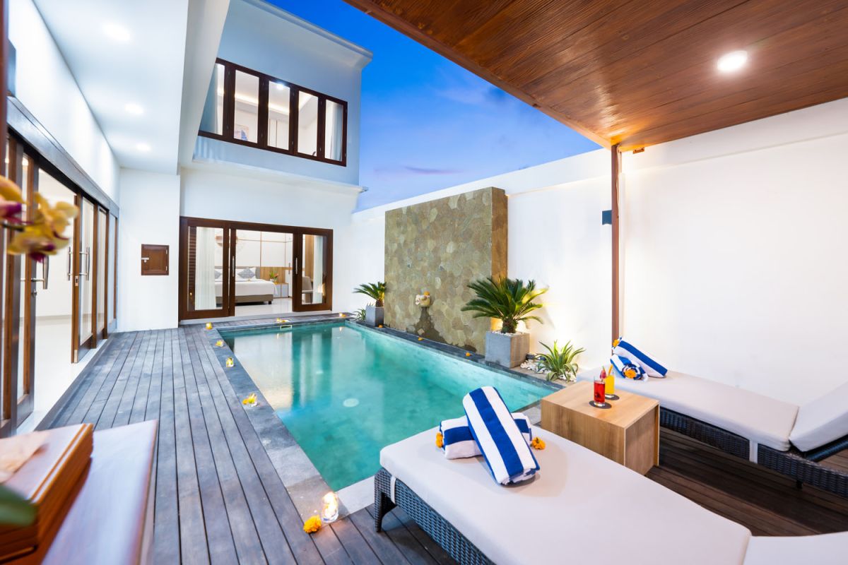 Luxurious private infinity pool in a modern Balinese villa, with lounge chairs, tropical plants, and sunset lighting. - Bali Villas