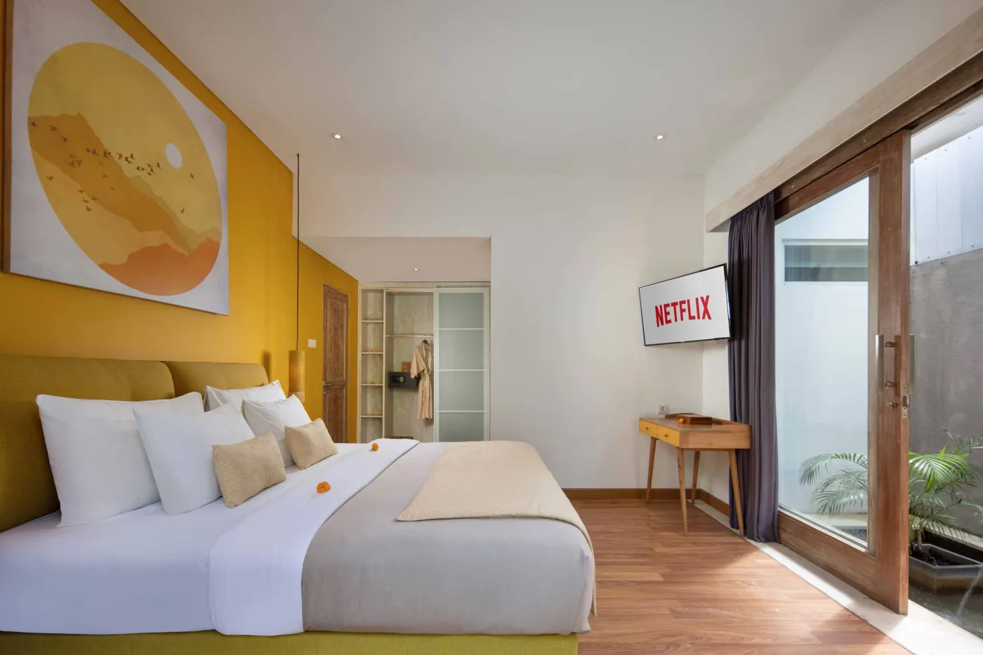 Modern Balinese villa bedroom with yellow accents, open sliding doors to a private turquoise pool, and lush tropical plants on a wooden deck. - Bali Villas