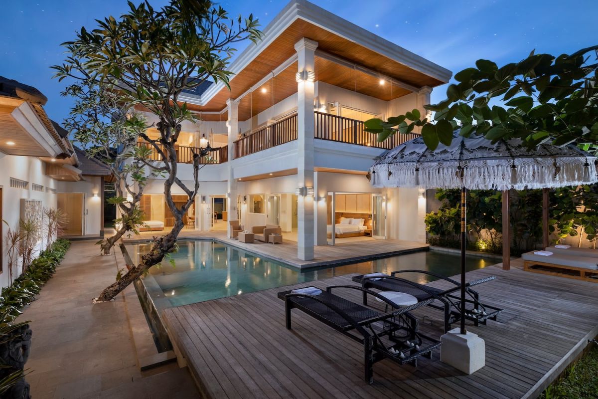 Elegant modern Balinese villa with private infinity pool, wooden deck, loungers, and lush tropical greenery at dusk. - Bali Villas