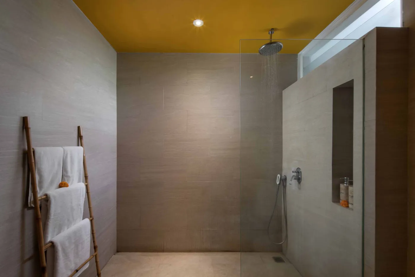 Modern Balinese villa bedroom with yellow accents, open sliding doors to a private turquoise pool, and lush tropical plants on a wooden deck. - Bali Villas