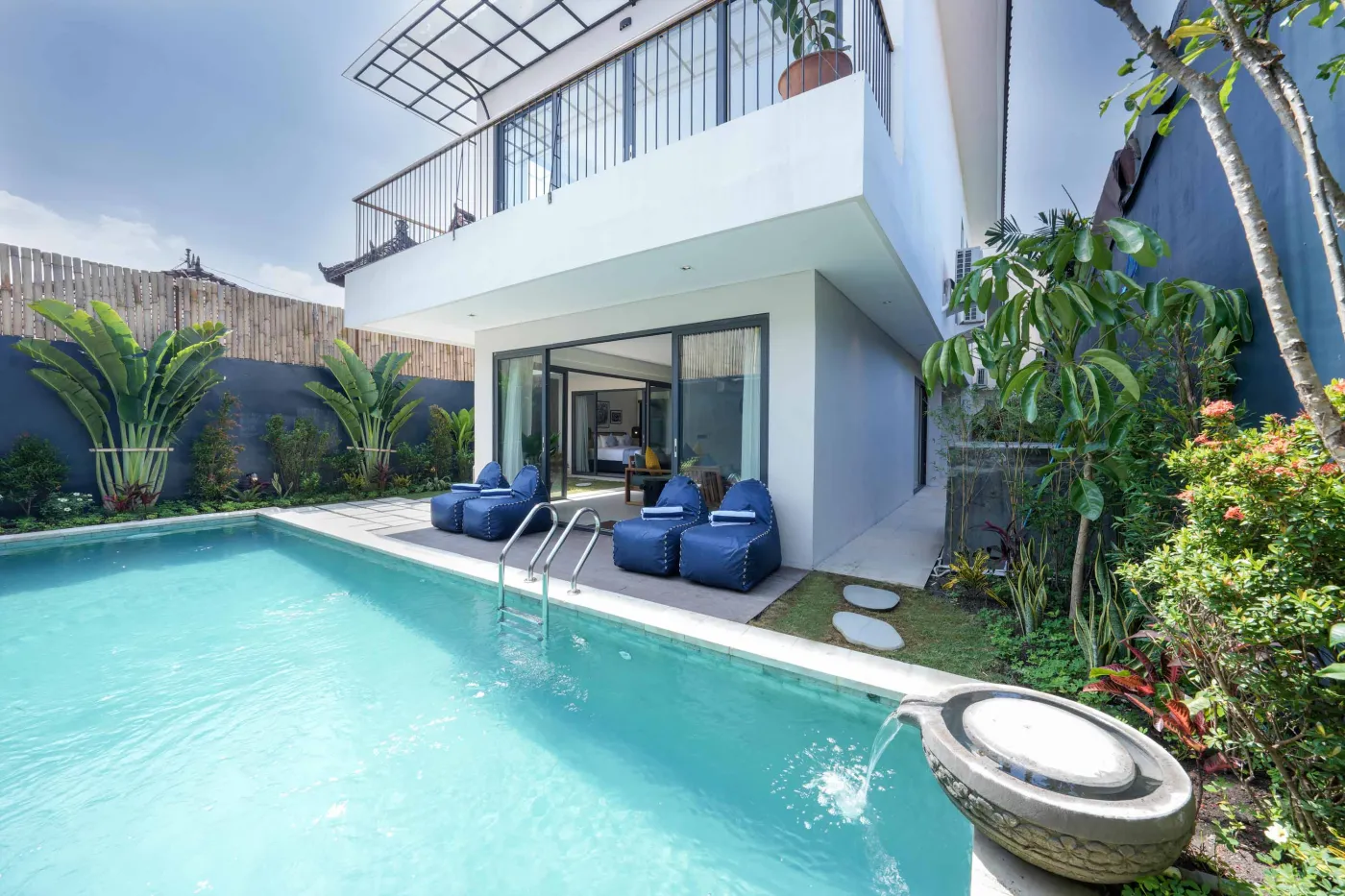 Modern Bali villa with turquoise infinity pool, blue lounge chairs, and lush tropical garden. - Bali Villas