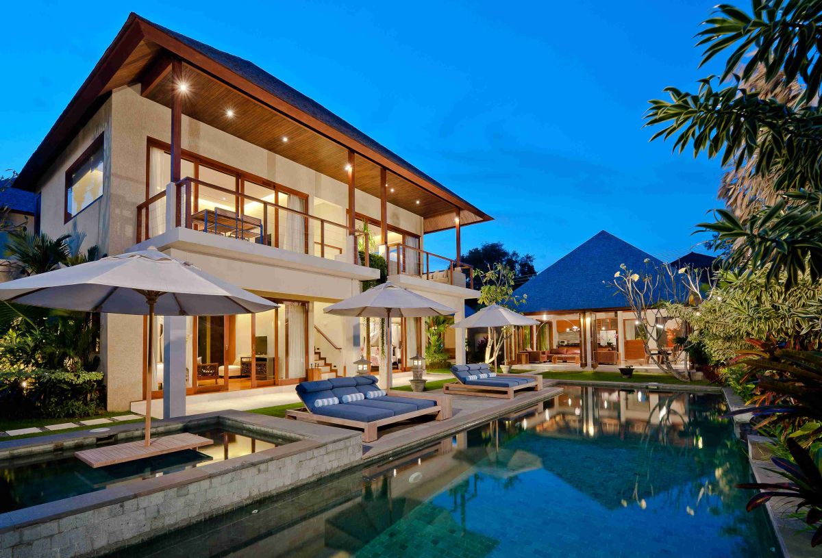 Luxurious Bali-style villa at dusk with infinity pool, loungers, and tropical gardens. - Bali Villas