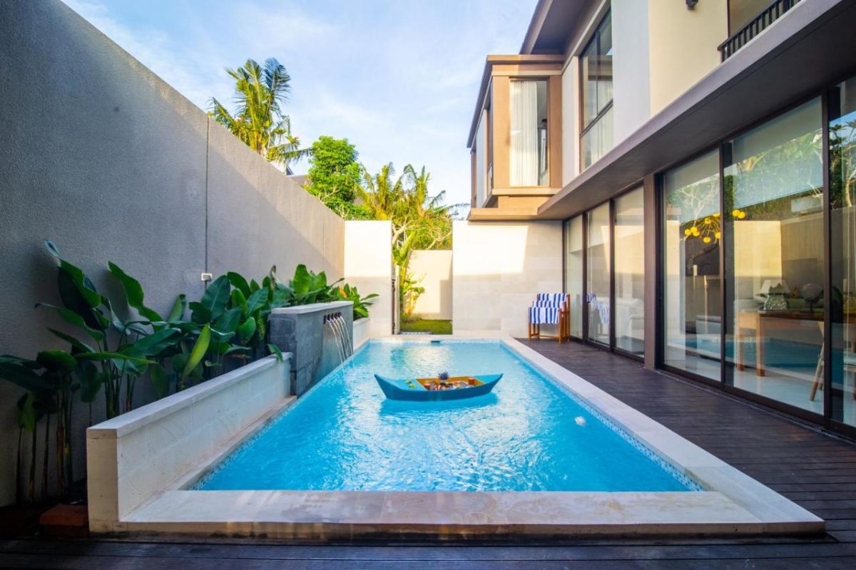 Modern tropical villa infinity pool with floating boat, lush greenery, and sleek glass architecture in Bali sunset light. - Bali Villas