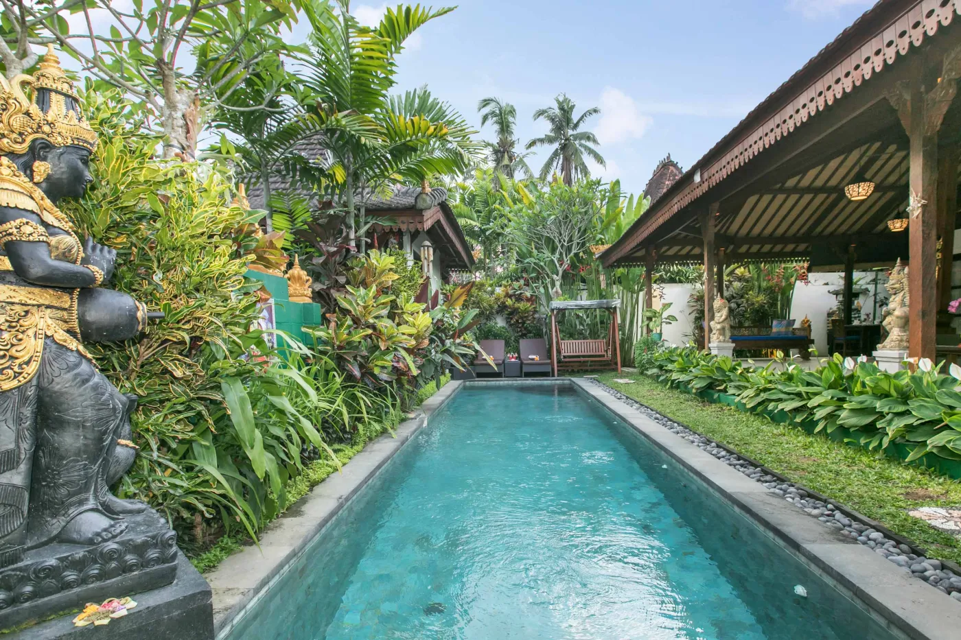 Serene infinity pool in a lush tropical Balinese garden, flanked by golden deity statue and traditional wooden pavilions. - Bali Villas