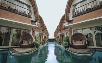 Luxurious tropical infinity pool flanked by thatched-roof villas and hanging lounge chairs with serene water reflections. - Bali Villas