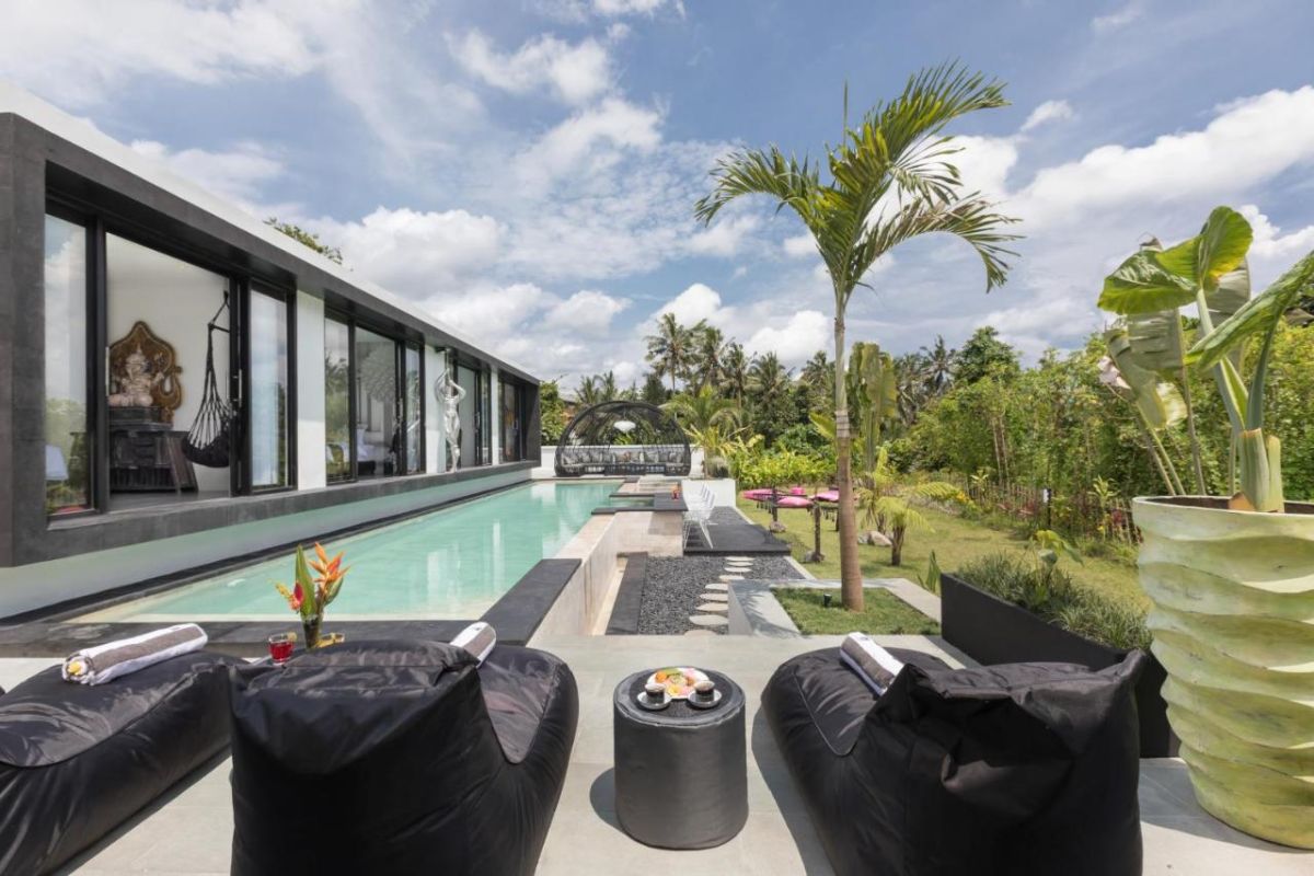 Modern luxury Bali villa with infinity pool, tropical palm surroundings, and black bean bag loungers on a deck overlooking lush greenery. - Bali Villas