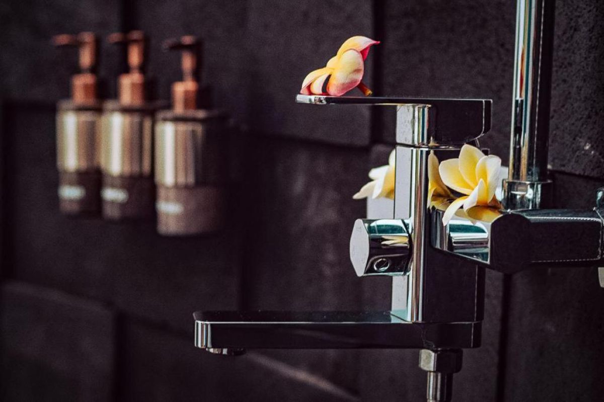 Modern outdoor shower with black pebble walls, tropical plants, hanging towels, and a sleek white sink. - Bali Villas