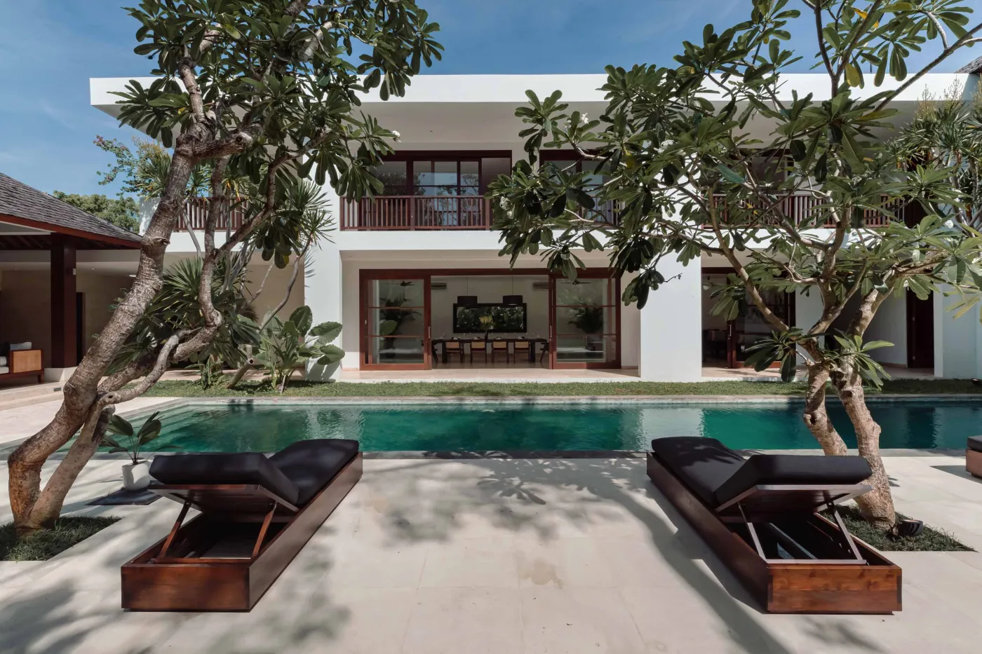 Modern white tropical villa with infinity pool, lounge chairs, and palm trees. - Bali Villas