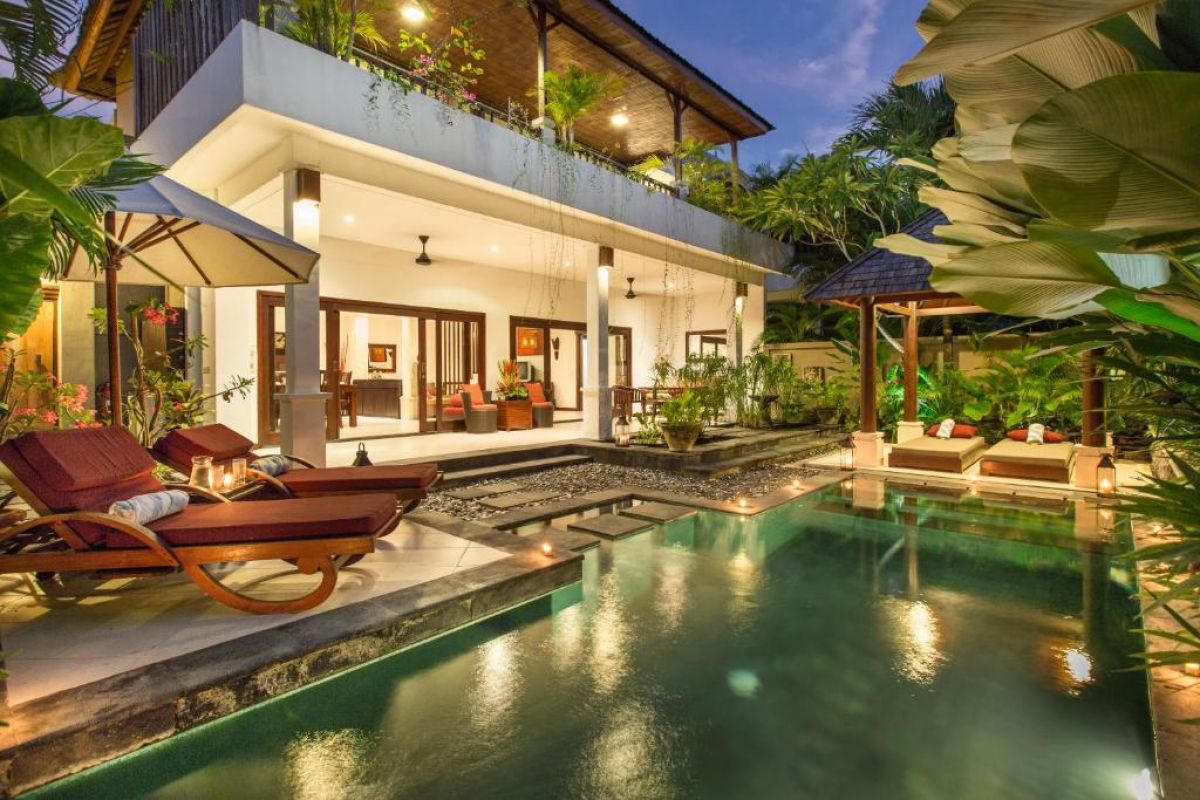 Luxurious Balinese villa with glowing infinity pool, lounge chairs, and tropical garden at dusk. - Bali Villas
