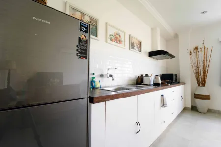 Modern white kitchen interior with wooden countertop, stainless steel sink, toaster, microwave, and Polystar refrigerator. - Bali Villas