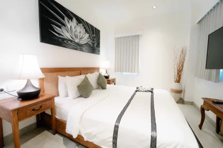 Serene Balinese-style bedroom with wooden bed, white linens, black-and-white lotus wall art, table lamps, and bamboo decor.