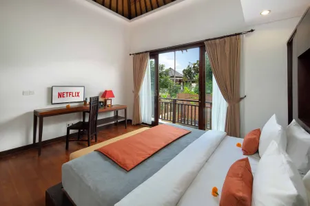 Cozy Balinese villa bedroom with Netflix desk, king bed with orange accents, and tropical garden view.