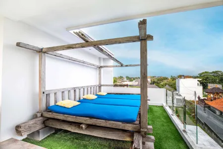 Rustic wooden daybed with blue cushions on a lush rooftop terrace, overlooking tropical cityscape. - Bali Villas