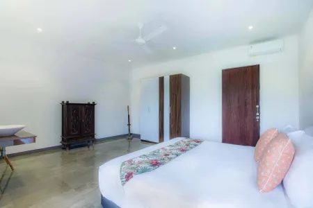 Spacious Balinese-style bedroom featuring a king bed with floral runner, wooden wardrobes, ceiling fan, and modern air conditioning.