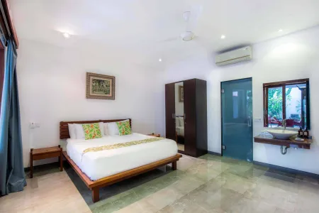 Spacious Balinese villa bedroom with wooden platform bed, green pillows and curtains, mirrored wardrobe, and open en-suite bathroom.