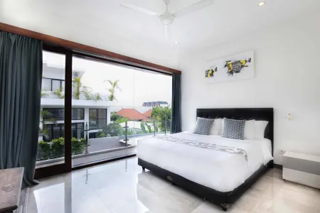 Luxurious tropical bedroom with king-sized bed, ceiling fan, and floor-to-ceiling glass doors overlooking palm trees and villa gardens.