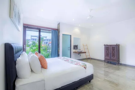 Spacious tropical bedroom with king bed, wooden accents, vanity, and lush garden view through sliding doors.