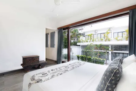 Modern tropical bedroom with white linens on a king bed, wooden accents, and sliding glass doors to lush garden view.