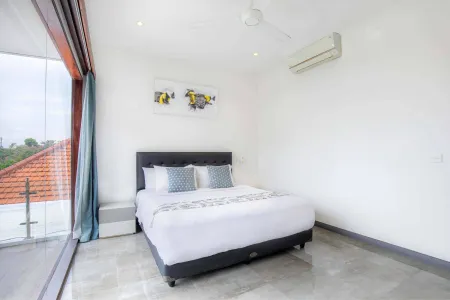 Spacious modern bedroom in tropical villa with king bed, white linens, balcony view of red-tiled roofs, ceiling fan, and abstract fish wall art.