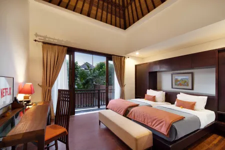 Luxurious Balinese villa bedroom with wooden beamed ceiling, twin beds in orange linens, balcony view of tropical greenery, and modern desk setup.