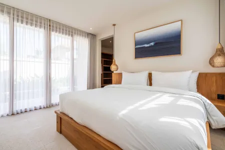 Serene luxury bedroom with wooden king bed, white linens, sheer window curtains, and abstract ocean wave painting.