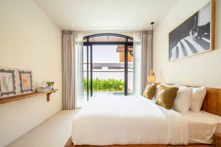 Spacious modern bedroom with king bed, sheer curtains, wall art, and arched sliding doors opening to tropical garden view.