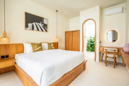 Modern tropical bedroom with wooden platform bed, neutral linens, rattan pendant lamps, and arched doorway to greenery
