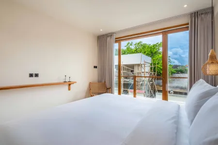 Serene tropical bedroom with king bed, wooden accents, and open sliding doors revealing a lush riverside view at dusk.