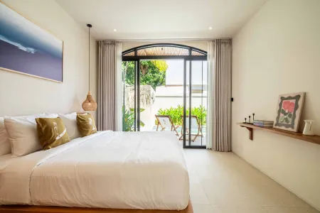 Spacious modern bedroom with king bed, open sliding doors to tropical garden balcony, and minimalist decor.