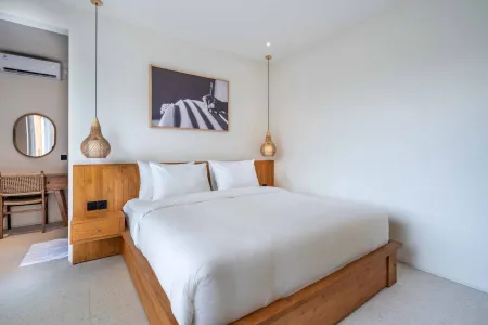 Cozy minimalist bedroom with wooden platform bed, white linens, rattan pendant lights, and abstract black-and-white wall art.