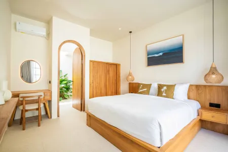 Spacious tropical bedroom with wooden platform bed, ocean wave artwork, arched door to lush garden, and rattan pendant lights. - Bali Villas