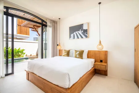 Modern tropical bedroom with wooden platform bed, white linens, pendant lamps, and open glass doors to a private pool.