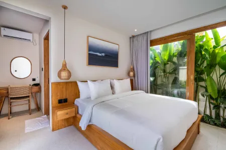 Spacious Balinese bedroom with wooden king bed, white bedding, rattan lamps, and sliding doors to tropical plants.