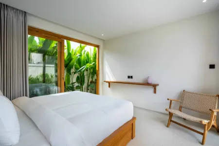Modern minimalist bedroom with white bed, tropical plants behind wooden sliding doors, wall shelf with vase, and rattan chair.