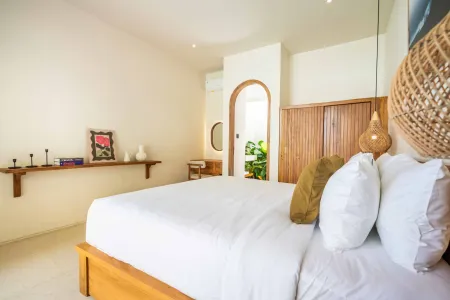 Serene minimalist bedroom with white wooden bed, rattan pendant light, wooden shelf decor, and arched doorway to ensuite.