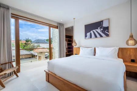 Spacious tropical bedroom in a Bali villa with wooden bed, white linens, bamboo lights, and panoramic views of palm trees and sunset sky.