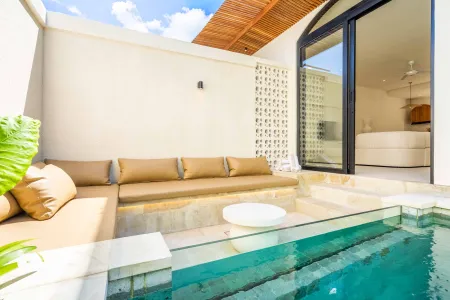 Modern tropical villa terrace featuring a private turquoise pool, beige L-shaped lounge sofa, potted plants, and sliding glass doors to a white bedroom, under a partly cloudy blue sky.