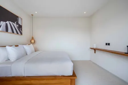 Minimalist white bedroom with wooden platform bed, plush pillows, large black-and-white wall art, and hanging lantern pendant light.
