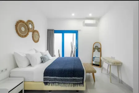 Cozy bohemian bedroom interior with white king bed, blue patterned duvet, rattan wall hangings, wooden vanity, and blue sliding doors to balcony.