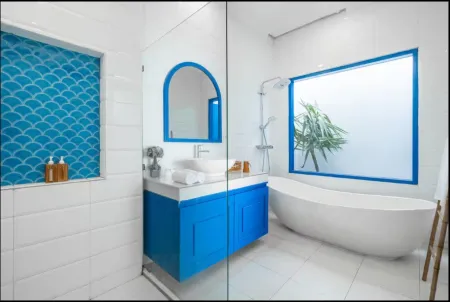 Modern bathroom with white tiles, blue mosaic shower, arched mirror over sink, freestanding tub, and potted plant. - Bali Villas