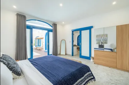 Spacious modern bedroom with blue arched doors open to outdoor patio, king bed in blue duvet, mirrored wardrobe, and neutral decor.