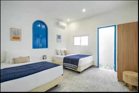 Bright twin-bed bedroom with blue arched window, navy bedding, white walls, and modern tropical decor.