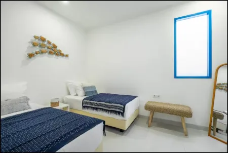 Cozy minimalist twin bedroom with blue bedding, wooden fish wall art, rattan bench, and arched mirror.