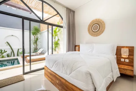 Serene tropical bedroom with wooden bed, white linens, and sliding doors to a private poolside garden. - Bali Villas